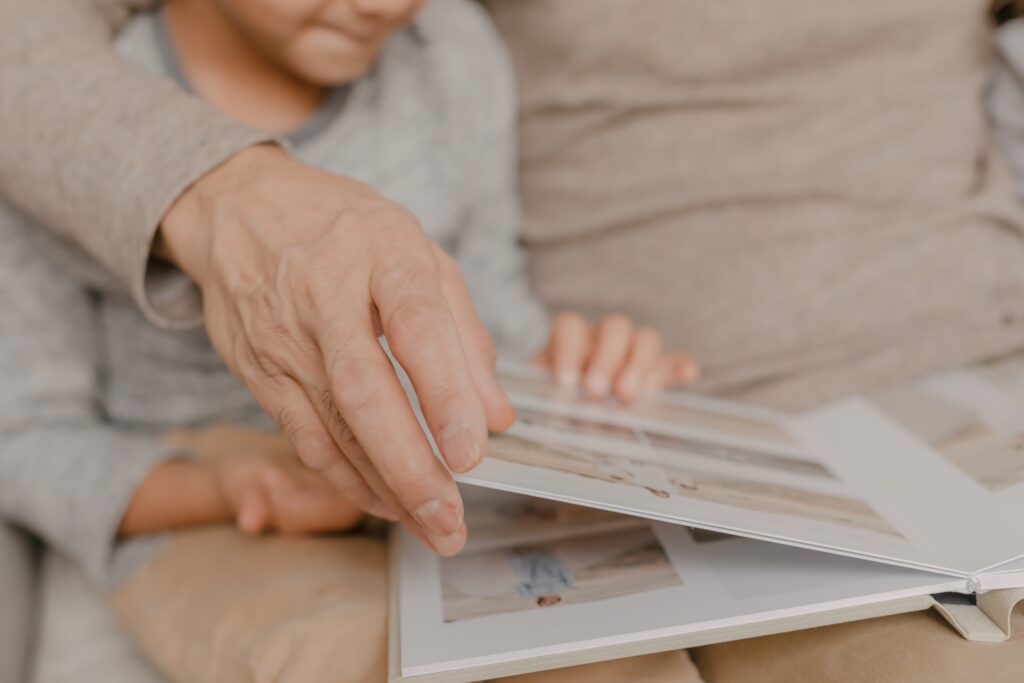 hand of an elder man flipping through photography album with grandchild on lap