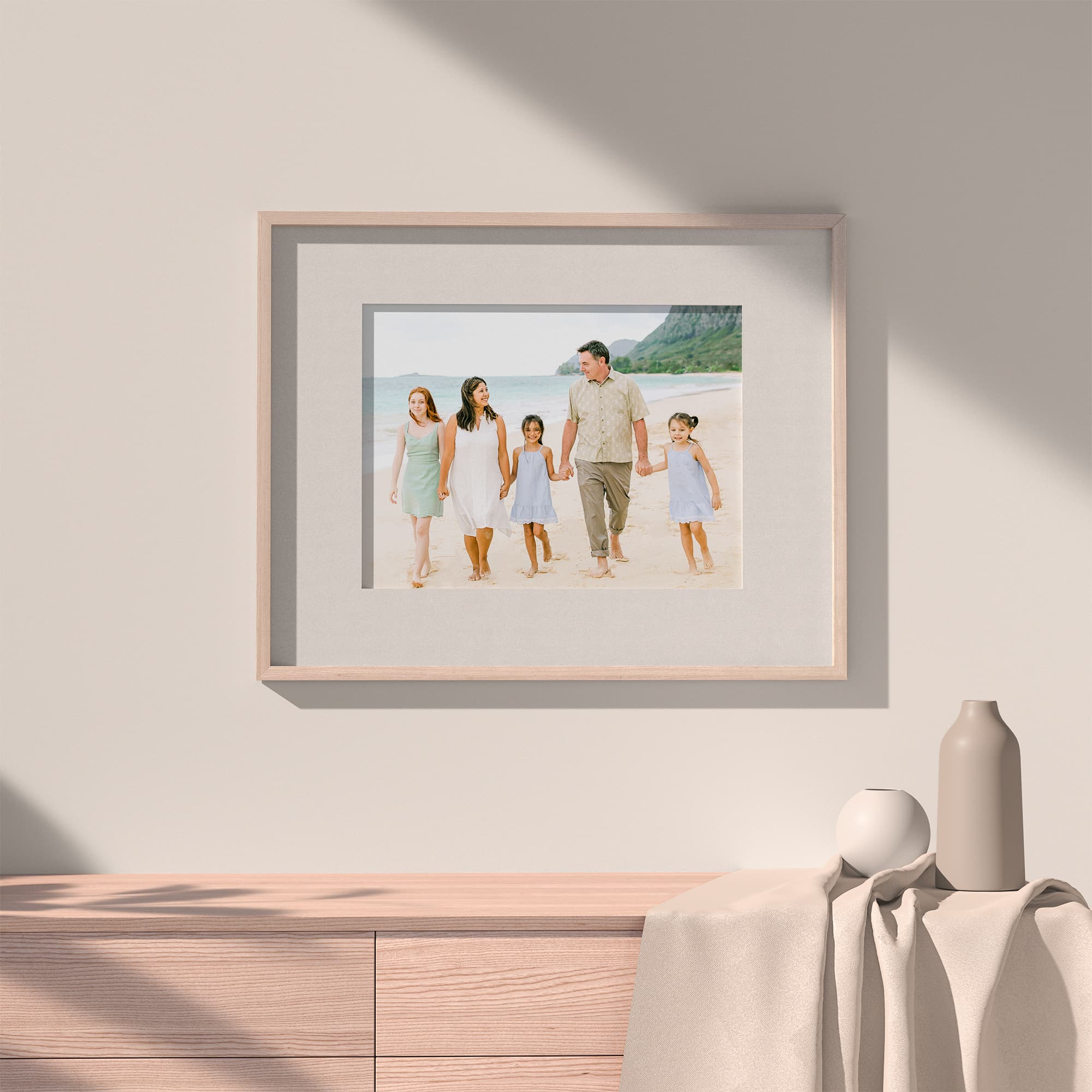 A framed image of a family of 5 walking on a beach hangs on a wall above a dresser