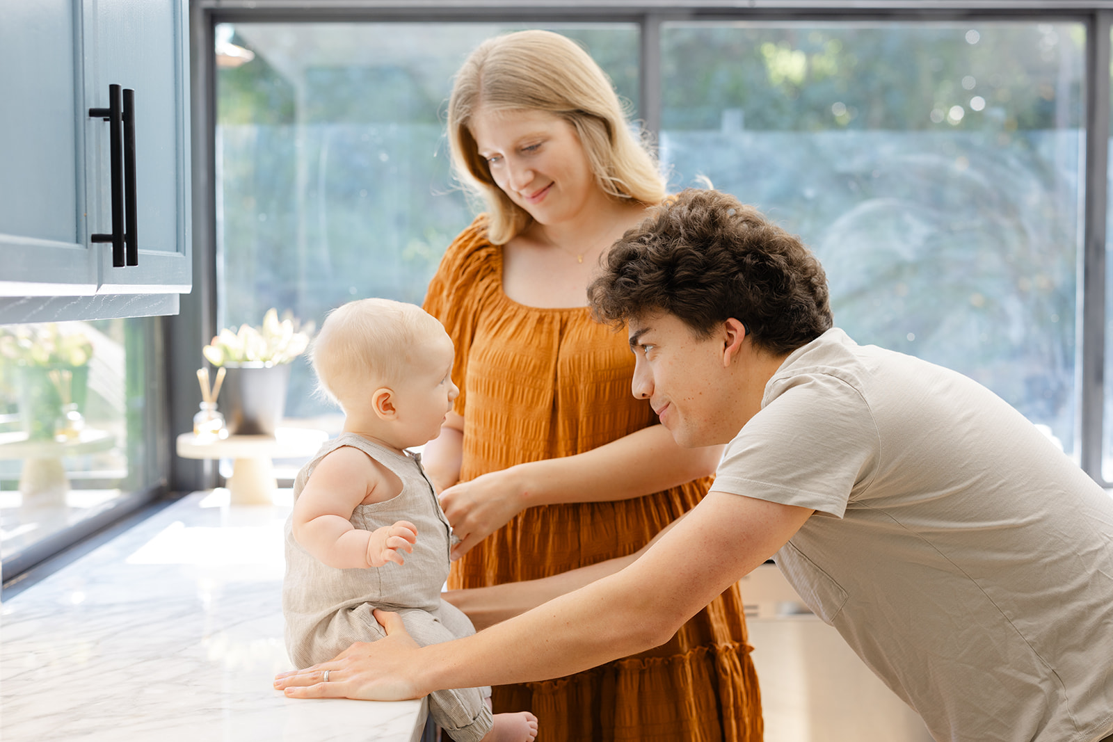 A mother and father play with their infant son while sitting on a kitchen counter