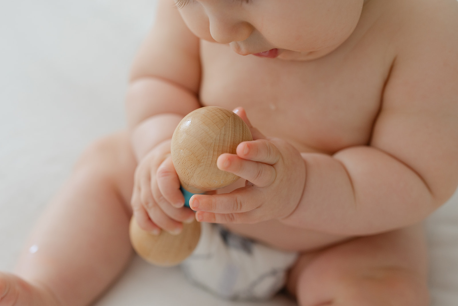 An infant baby sits on a bed playing with a wooden toy before meeting Irvine Pediatricians