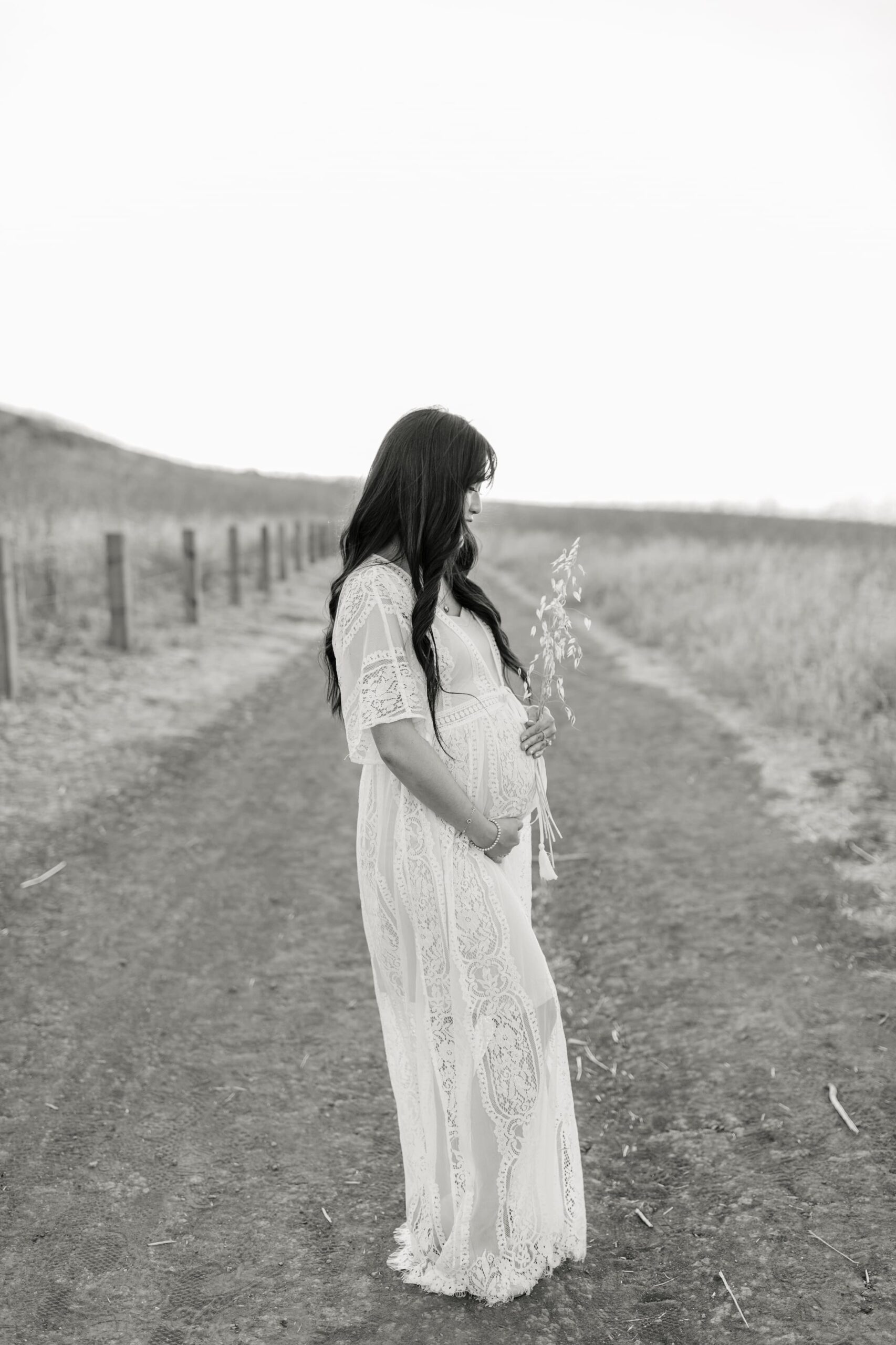 Black and white image of a pregnant woman in a lace dress holding her bump after finding an obgyn orange county