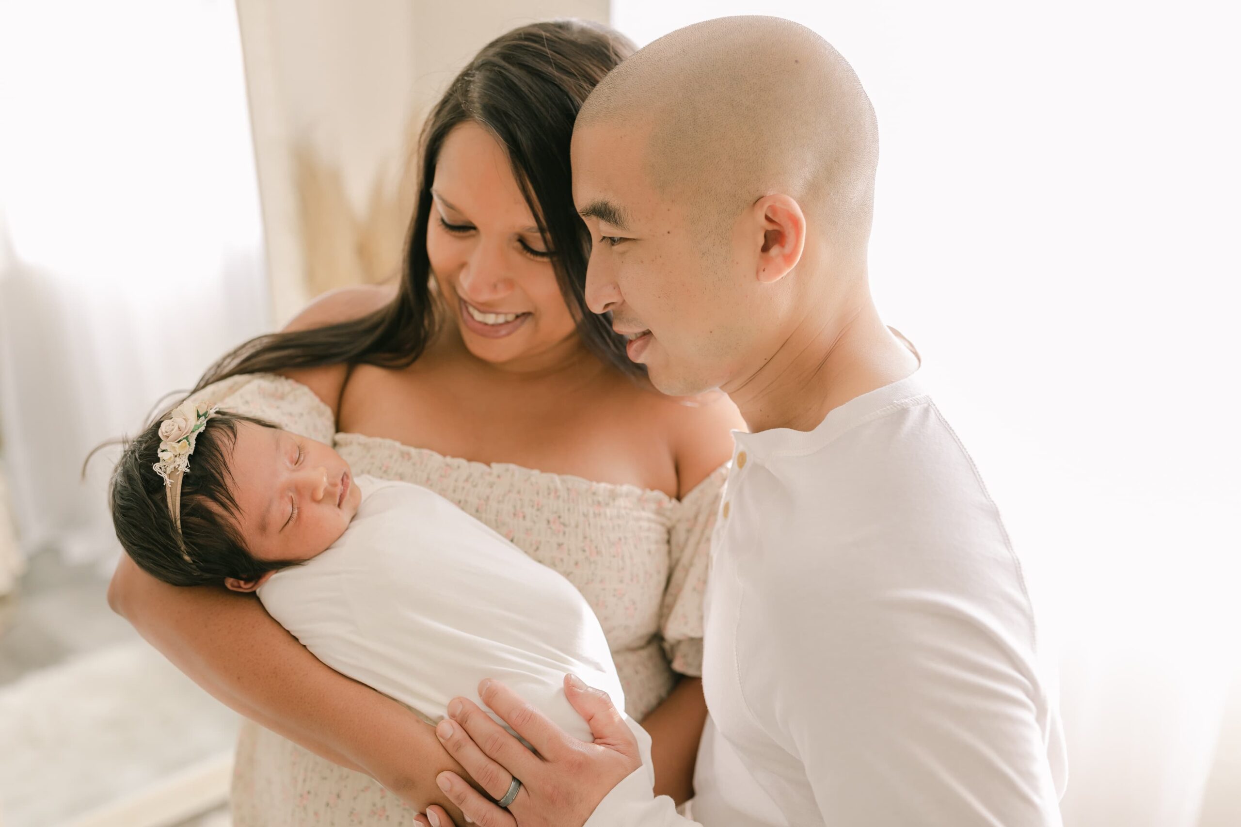 Happy new parents smile down at their newborn baby in mom's arms while standing by a mirror thanks to orange county birth center