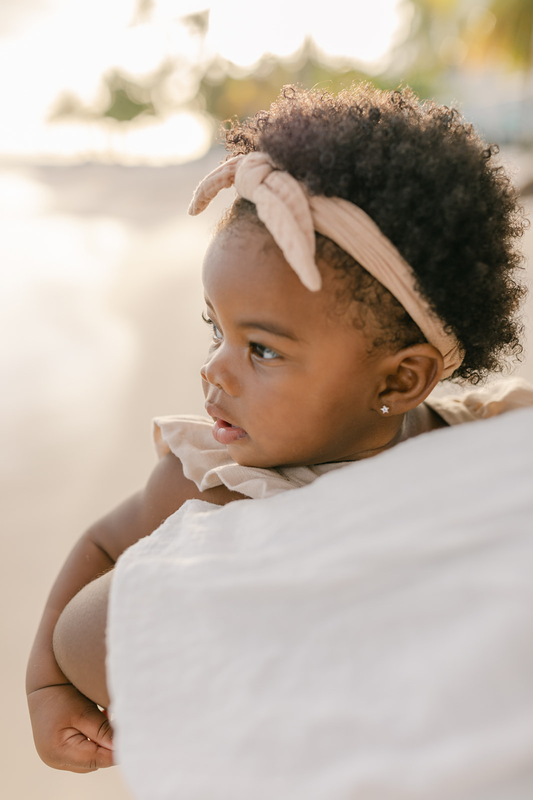 A toddler girl sits in mom's arms while walking up a beach at sunset before meeting an orange county Pediatrician