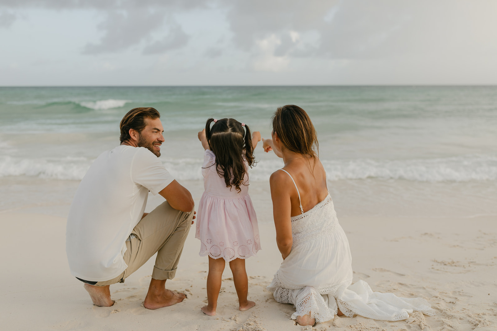 A mother and father explore the beach and ocean waves in white and pink