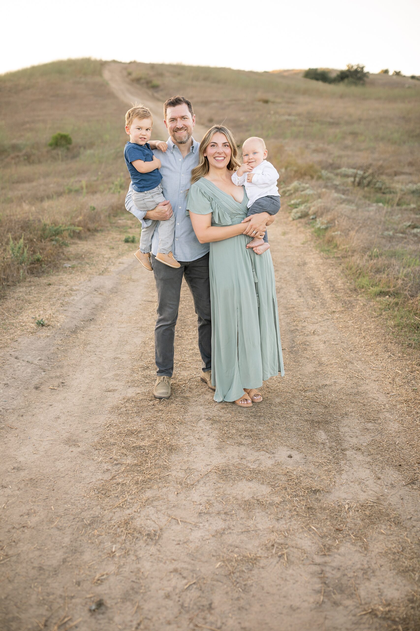 Happy parents stands in a park trail holding their two toddler sons on their hips during things to do in orange county with toddlers