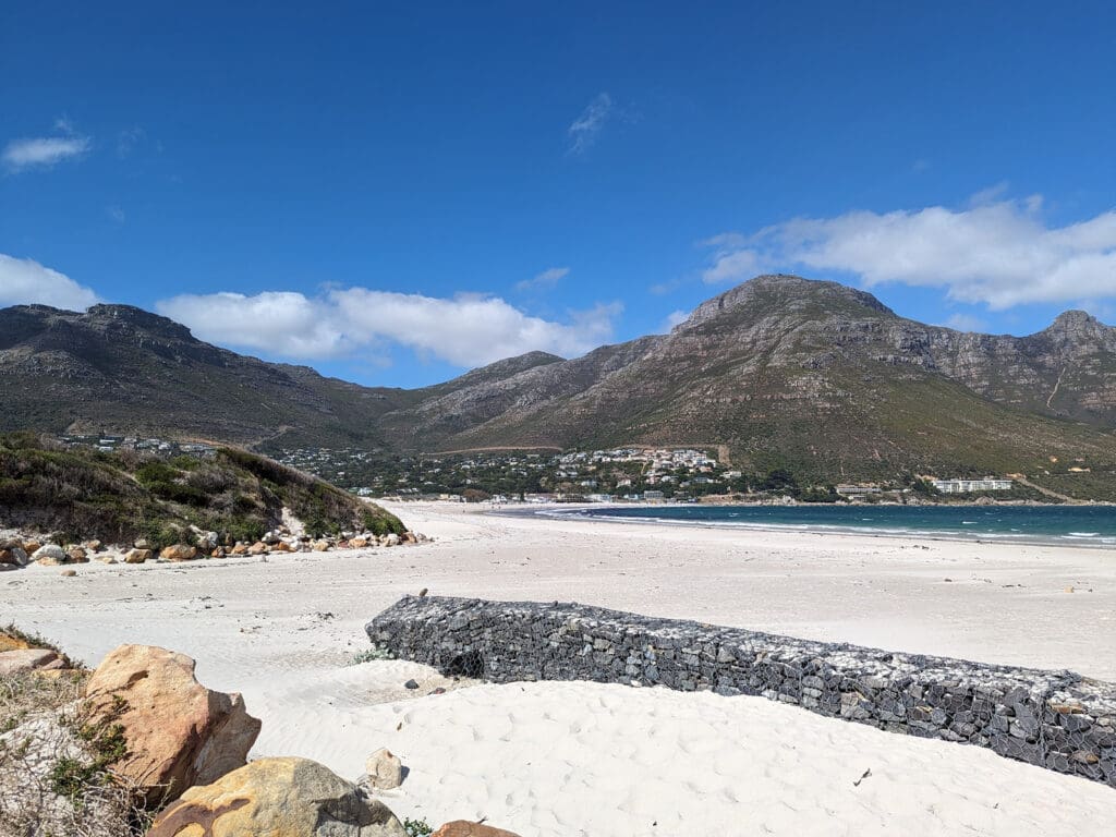 Hout Bay Beach, South Africa, has white sand with mountains and aqua green water.