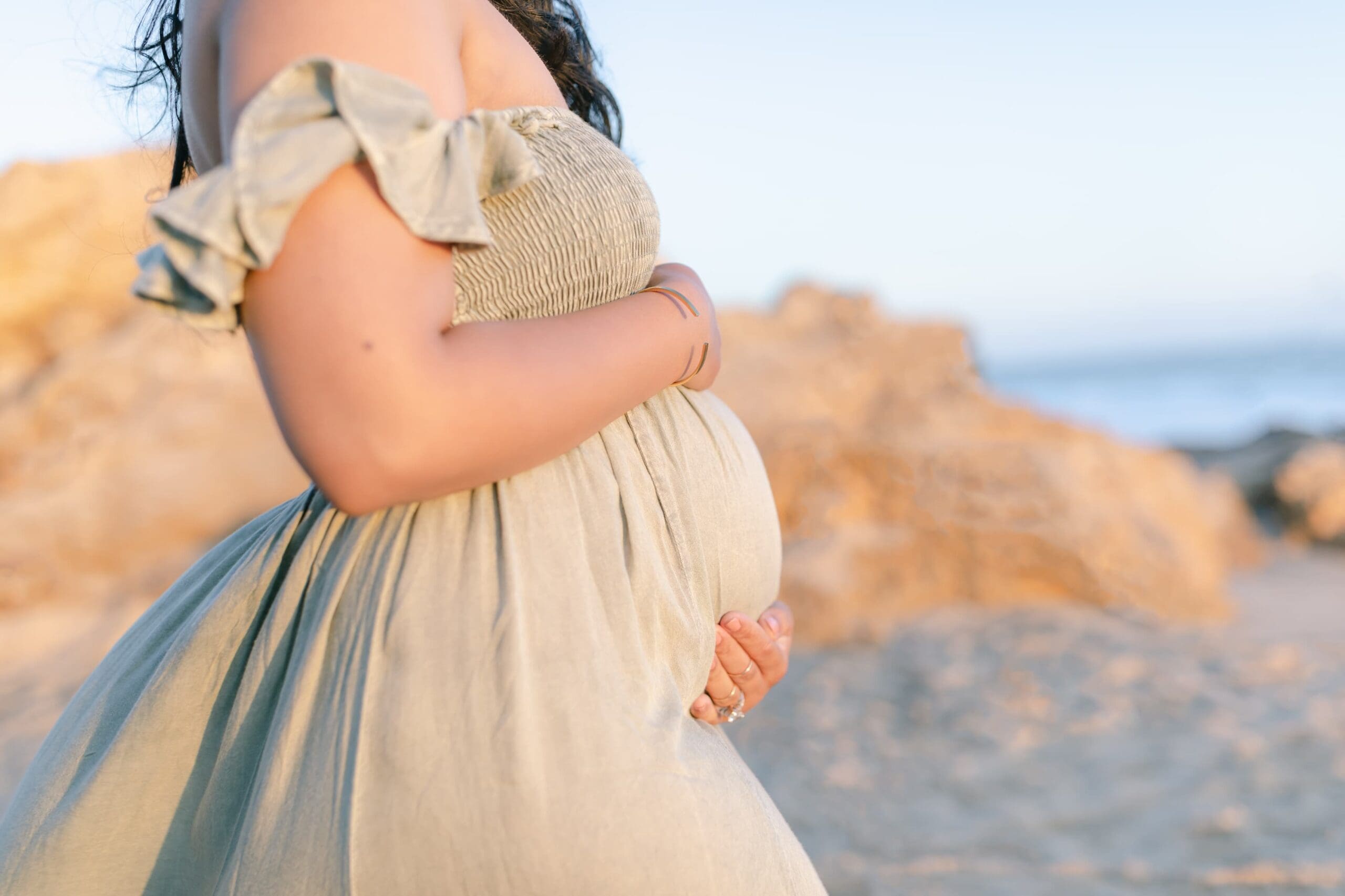 Pregnant woman on a beach in newport beach holding her belly